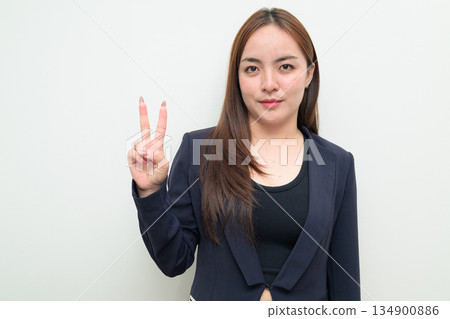 Portrait of a young Asian businesswoman against white background making peace sign gesture Portrait of a young Asian businesswoman against white background making peace sign gesture 134900886
