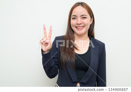 Portrait of a young Asian businesswoman against white background making peace sign gesture Portrait of a young Asian businesswoman against white background making peace sign gesture 134900887