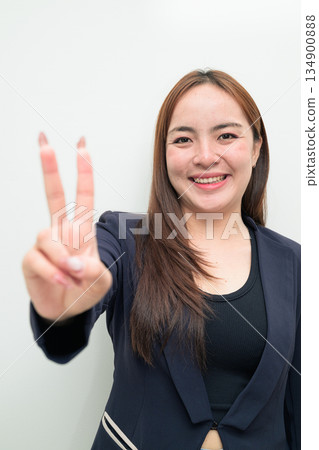 Portrait of a young Asian businesswoman against white background making peace sign gesture 134900888