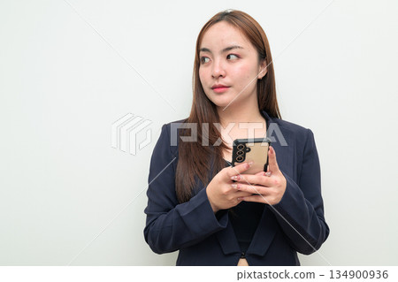 Portrait of a young Asian businesswoman against white background using phone thinking 134900936