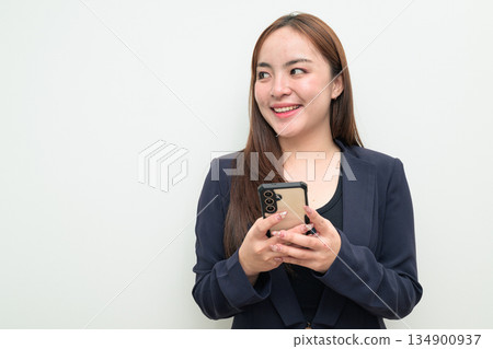 Young happy Asian businesswoman against white background using phone smiling and thinking 134900937