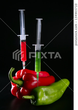 Injection with syringe to red and green peppers over black background 134903710