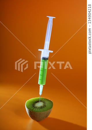 Injection with syringe to a green kiwi fruit over orange background 134904218