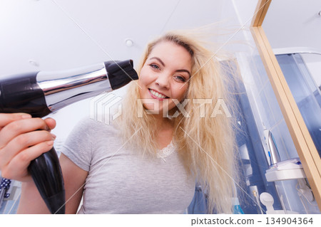 Woman drying hair in bathroom Woman drying hair in bathroom 134904364