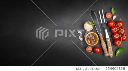 Cooking background with fresh cherry tomatoes, spices, cutlery and herbs on black slate surface with copy space 134904836