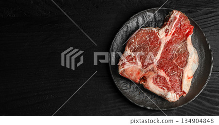 Raw t-bone beef steak on black plate over dark wooden background with copy space for restaurant menu or butcher advertising 134904848