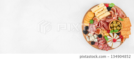 Top view of gourmet charcuterie board with cheese, prosciutto, olives, crackers and fresh berries on white background with copy space Top view of gourmet charcuterie board with cheese, prosciutto, olives, crackers and fresh berries on white background with copy space 134904852