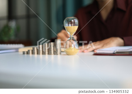 Rising stack of coins and running sand clock on the table. Growing of income, saving or return investment through time. Time and money concept. Rising stack of coins and running sand clock on the table. Growing of income, saving or return investment through time. Time and money concept. 134905332