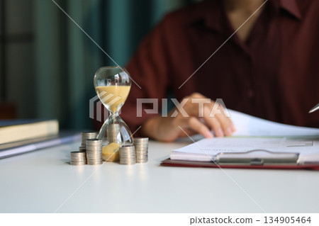 Coin stacks and sand clock on the table. Growing of income, saving or return investment through time. Time and money concept. 134905464