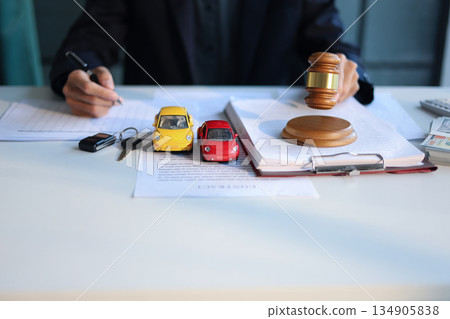 A man working on desk with gavel, contracts, and toy cars. Concept for Car Auction Legalities or Vehicle Bidding and Contracts. A man working on desk with gavel, contracts, and toy cars. Concept for Car Auction Legalities or Vehicle Bidding and Contracts. 134905838