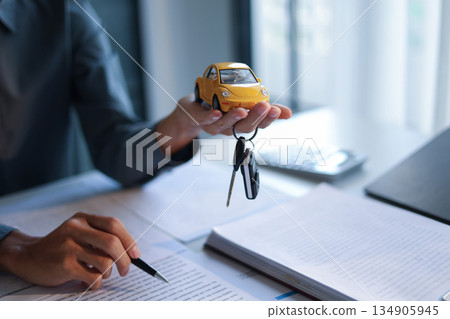 Car model and car key in hand. Concept for car loan, lease, insurance, buying or selling. Car model and car key in hand. Concept for car loan, lease, insurance, buying or selling. 134905945