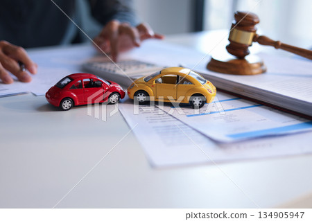 A man working on desk with gavel, contract and toy cars. Concept for Car Auction Legalities or Vehicle Bidding and Contracts. A man working on desk with gavel, contract and toy cars. Concept for Car Auction Legalities or Vehicle Bidding and Contracts. 134905947