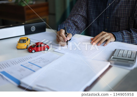 A man signing a contract for a car loan, lease, vehicle registration or insurance policy. Concept for Sales Contract, Financing Agreement, Insurance Policy, Vehicle Registration. A man signing a contract for a car loan, lease, vehicle registration or insurance policy. Concept for Sales Contract, Financing Agreement, Insurance Policy, Vehicle Registration. 134905958