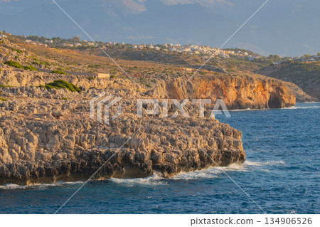 stunning cretan coastal landscape with sheer rocky cliffs meeting blue sea and houses on the hill 134906526