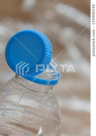 Water bottle cap is off and resting on top of an empty plastic bottle near crumpled plastic Water bottle cap is off and resting on top of an empty plastic bottle near crumpled plastic 134906549