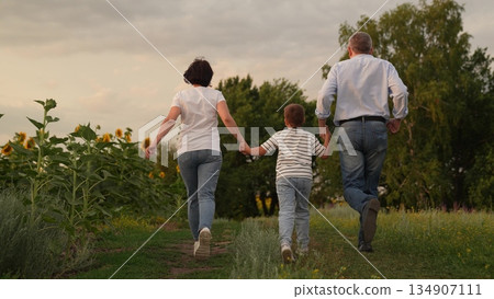 Family Walking in Nature, Grandparents with Grandchild Outdoors, Generations Together in Field, Peaceful Family Time, Holding Hands in Countryside, Spring or Summer Walk, Family Bonding Moments, Rural 134907111