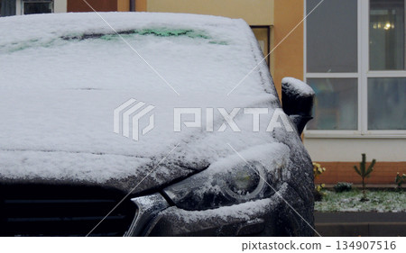 Headlight of gray car parked in front of residential building covered with snow and ice Headlight of gray car parked in front of residential building covered with snow and ice 134907516