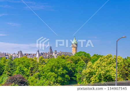 Luxembourg City historical centre with Tower of State Bank and Savings Bank Spuerkeess Banque et Caisse d'Epargne de l'Etat, Petrusse Parks green trees and blue sky background in sunny summer day 134907545