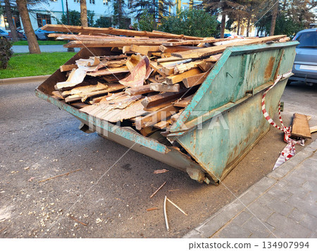 A large green open-top industrial waste container filled with construction debris stands outside in a residential yard 134907994
