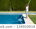 Girl cleaning swimming pool with skimmer net in 134910018