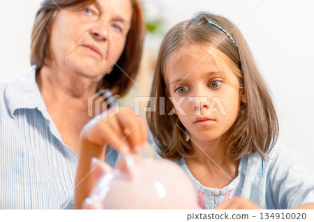 Granddaughter inserting coin into piggy bank while 134910020