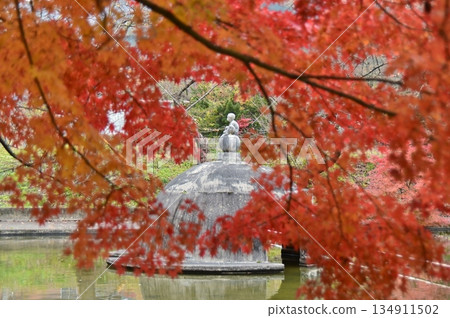 A stone statue seen through the red leaves of a maple tree A stone statue seen through the red leaves of a maple tree 134911502