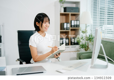 A focused office woman writing notes and working on paperwork at her desk, representing productivity, organization, business tasks, 134911509