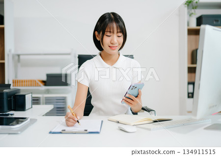 A focused office woman writing notes and working on paperwork at her desk, representing productivity, organization, business tasks, 134911515