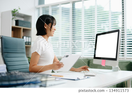 Confident Asian woman with a smile standing holding notepad and tablet at the modern office. 134911573