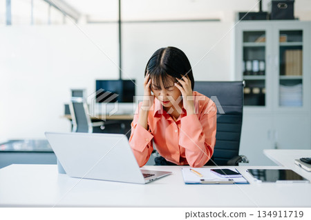 Stressed Asian Businesswoman Feeling Overworked at office desk with laptop. 134911719