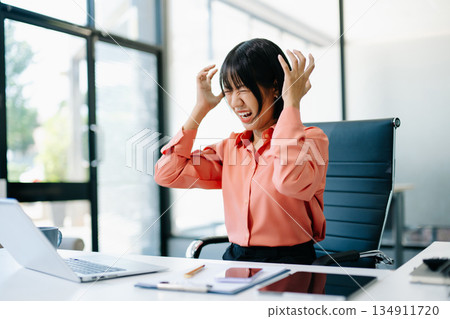 Stressed Asian Businesswoman Feeling Overworked at office desk with laptop. 134911720