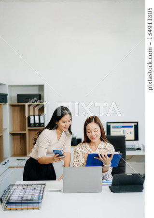 Businesswomen work and discuss their business plans. A woman employee explains and shows her colleague Businesswomen work and discuss their business plans. A woman employee explains and shows her colleague 134911805
