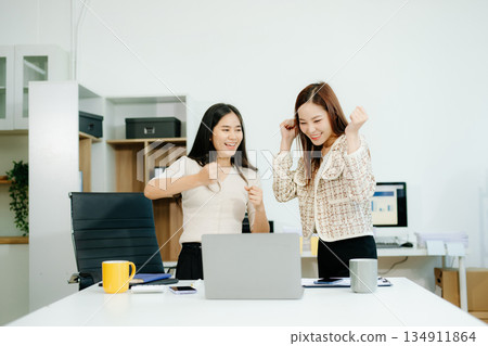Asian businesswomen enjoying coffee and teamwork at office desk while working on laptop. Great for themes of success, collaboration 134911864