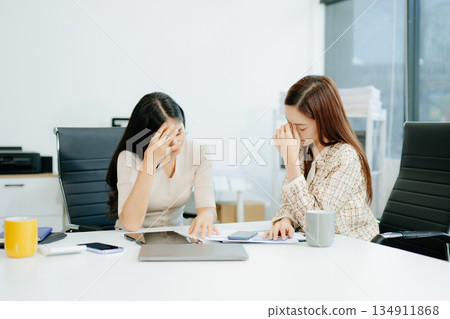 Asian woman comforts her distressed coworker in office. Concept of workplace stress, burnout, empathy, and emotional support in professional environments. 134911868