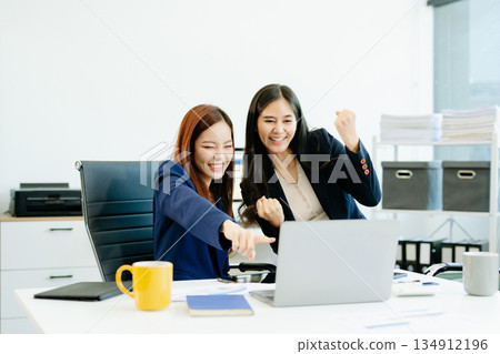 Two Asian businesswomen in suits analyze reports together at a modern office desk. A scene of teamwork, leadership Two Asian businesswomen in suits analyze reports together at a modern office desk. A scene of teamwork, leadership 134912196