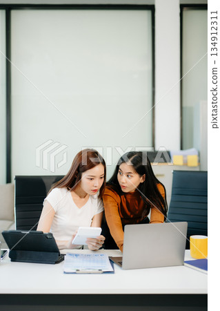 Businesswomen work and discuss their business plans. A woman employee explains and shows her colleague Businesswomen work and discuss their business plans. A woman employee explains and shows her colleague 134912311