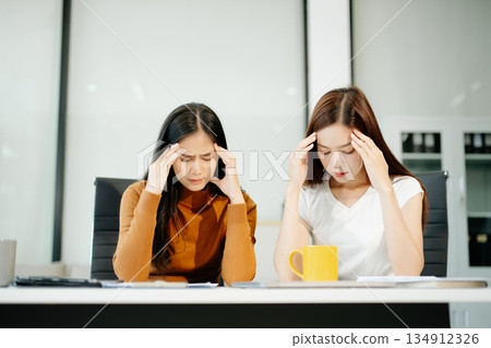Asian woman comforts her distressed coworker in office. Concept of workplace stress, burnout, empathy, and emotional support in professional environments. 134912326