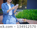 Young Asian Woman Using Smartphone Social Media App Sitting Outdoor with Coffee and Laptop Mobile Technology Connected Communication Relaxing Lifestyle 134912570