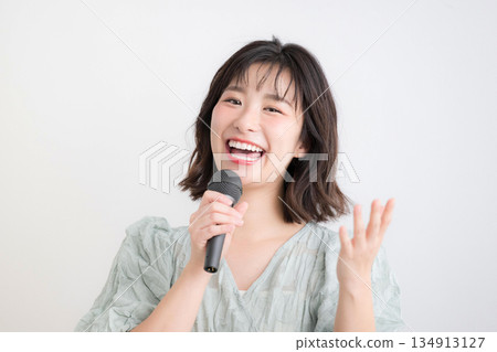 一位女士手持麥克風，正在上聲樂課、唱卡拉OK或接受聲樂訓練。圖片內容包括上課、主持等。 134913127