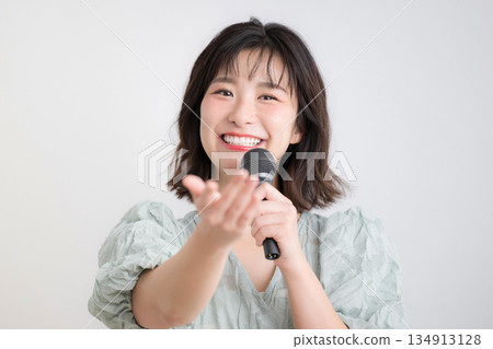 一位女士手持麥克風，正在上聲樂課、唱卡拉OK或接受聲樂訓練。圖片內容包括上課、主持等。 134913128