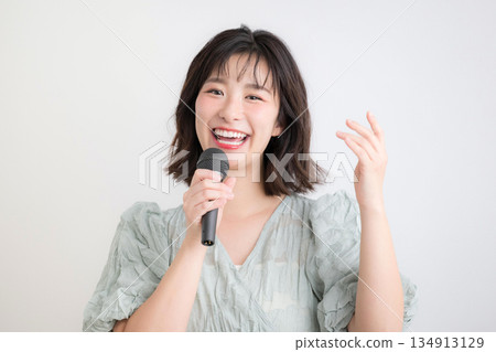一位女士手持麥克風，正在上聲樂課、唱卡拉OK或接受聲樂訓練。圖片內容包括上課、主持等。 134913129