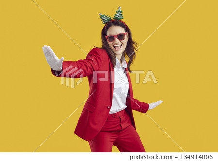Happy young woman in red suit and funny Christmas headband dancing on yellow background 134914006