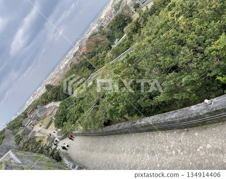 Shuri Castle walls and stone-paved slopes in Okinawa: Historical landscape overlooking the greenery and cityscape 134914406