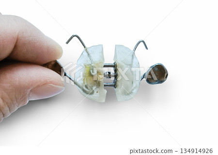 Close up of an orthodontist's hand holding a clear orthodontic retainer on a white background symbolizing a dental problem.  134914926