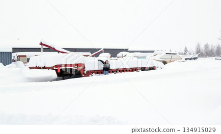 Grain farmer stands in the yard with equipment in heavy snow. 134915029