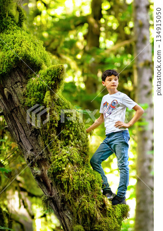 Teen boy is standing on the mossy tree trunk in the rainforest. Teen boy is standing on the mossy tree trunk in the rainforest. 134915050