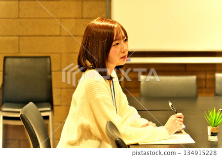 一位女員工在會議室、商務會議或面試場景中神情嚴肅地聆聽對方發言，同時做筆記。 134915228