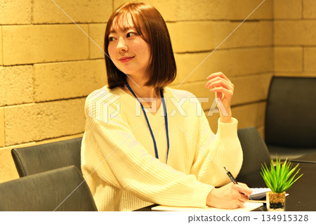 Young woman chatting with a colleague while using a calculator in the office 134915328