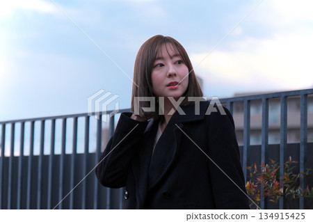 Woman in a black coat fixing her hair outdoors in the wind, winter evening portrait Woman in a black coat fixing her hair outdoors in the wind, winter evening portrait 134915425