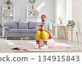 Funny upset man in sportswear sitting on fit ball holding dumbbells tired from hard workout at home 134915843